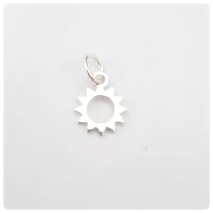 May include: A small, silver sun charm with a ring for attaching to a bracelet or necklace. The sun has a circular centre and pointed rays around the edge. The charm is displayed against a white background.