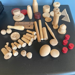 May include: A collection of wooden craft supplies, including dowels, spools, and blocks, in various shapes and sizes. There are also several red wooden rings.