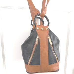 May include: Black and brown leather backpack with gold zippers and accents. The backpack has a rounded shape with a brown base and straps. The word "Valentina" is printed vertically on the front of the bag.