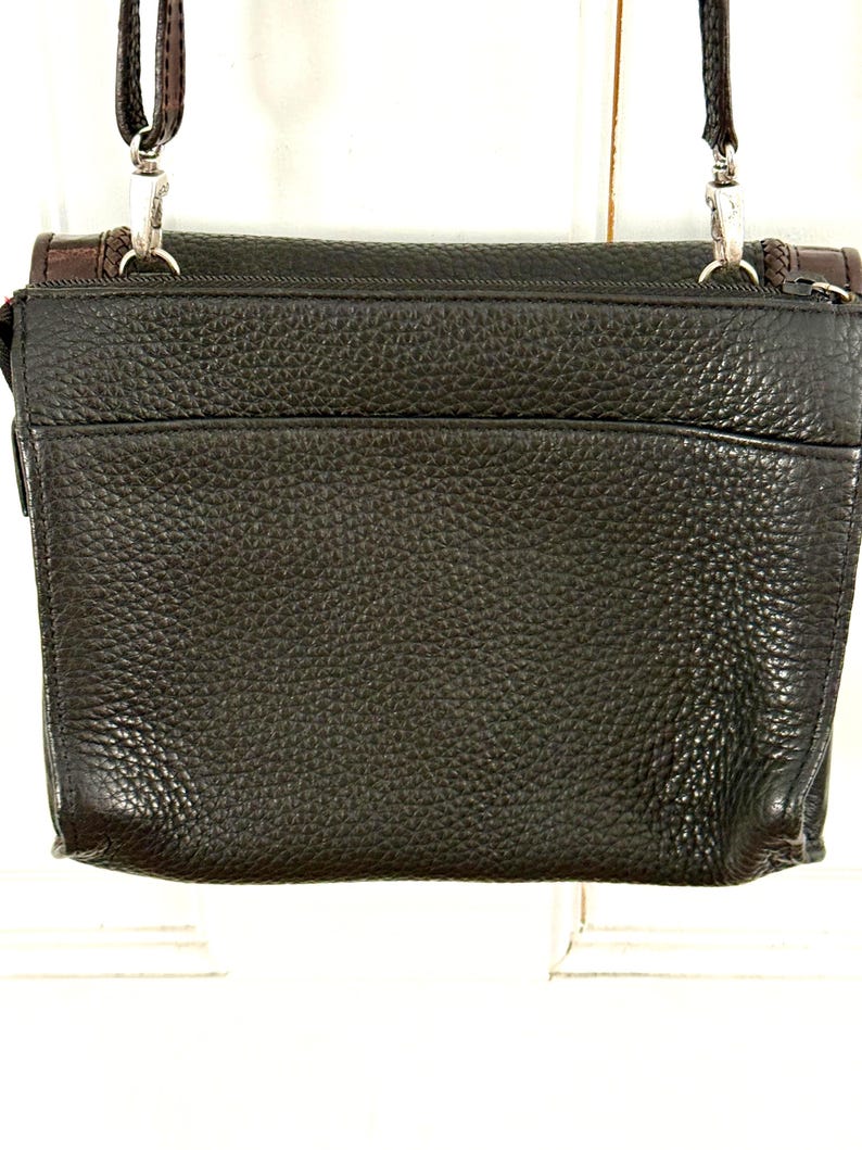 May include: A dark brown leather crossbody bag with a textured surface. The bag has a rectangular shape with a flap closure and a long, adjustable strap. Silver-tone hardware and brown accents are visible.
