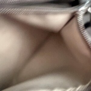 May include: A close-up of a light beige wallet, open to reveal the interior. The wallet has a silver zip and a textured, slightly shiny surface. The interior is a lighter shade of beige.