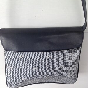 May include: A blue and white patterned shoulder bag with a black leather flap. The bag has a small logo on the front.