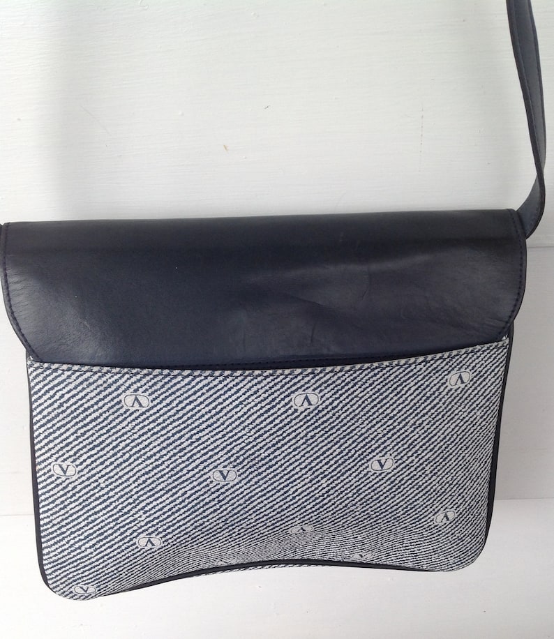 May include: A blue and white patterned shoulder bag with a black leather flap. The bag has a small logo on the front.