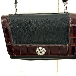 May include: Black and brown leather crossbody bag with a silver-tone clasp. The bag features a textured black leather center panel, framed by brown, crocodile-embossed leather. A silver-tone chain strap is attached.