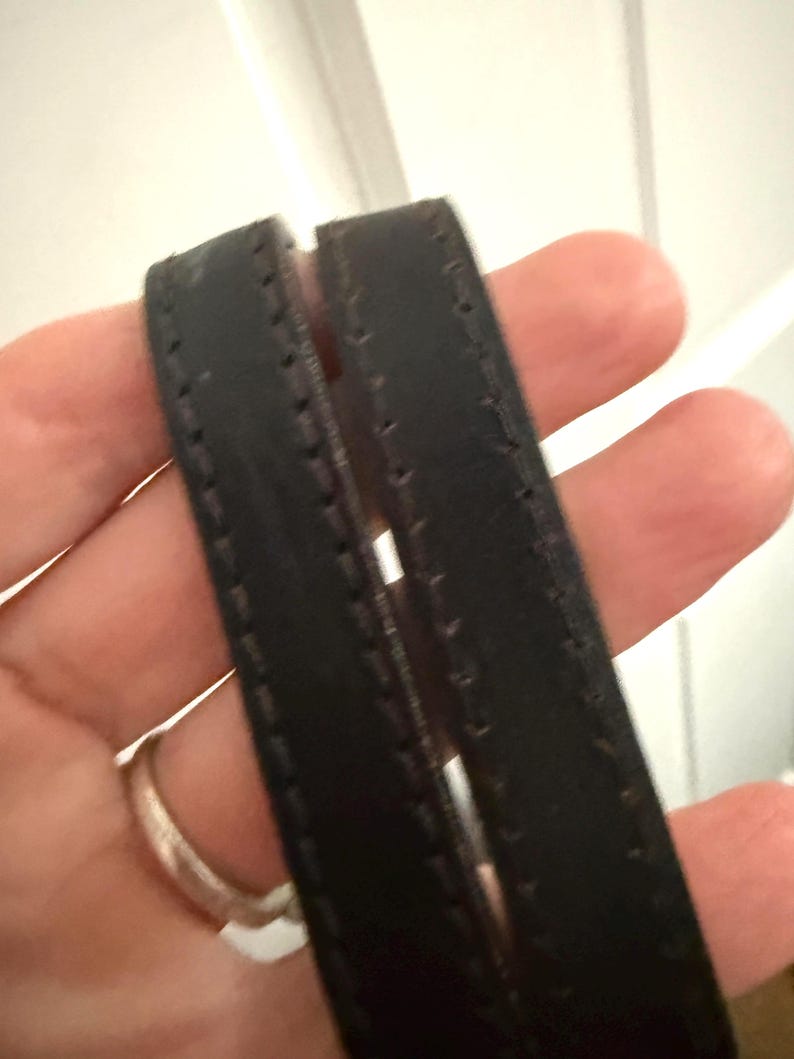 May include: Close-up of two black leather straps with visible stitching. The straps appear to be part of a handbag or tote, with a focus on the texture and craftsmanship of the material.