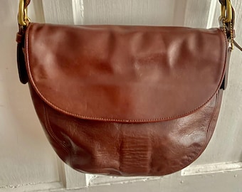 Bolso bandolera Coach Carlton marrón oscuro con forma de media luna.