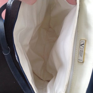 May include: The inside of a navy blue handbag with a white lining. The bag has a gold metal label that reads "valentino garavani made in italy".
