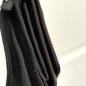 May include: Close-up of a black leather wallet with a silver chain. The wallet is folded, revealing a glimpse of the interior with a dark brown lining. The leather has a textured appearance.