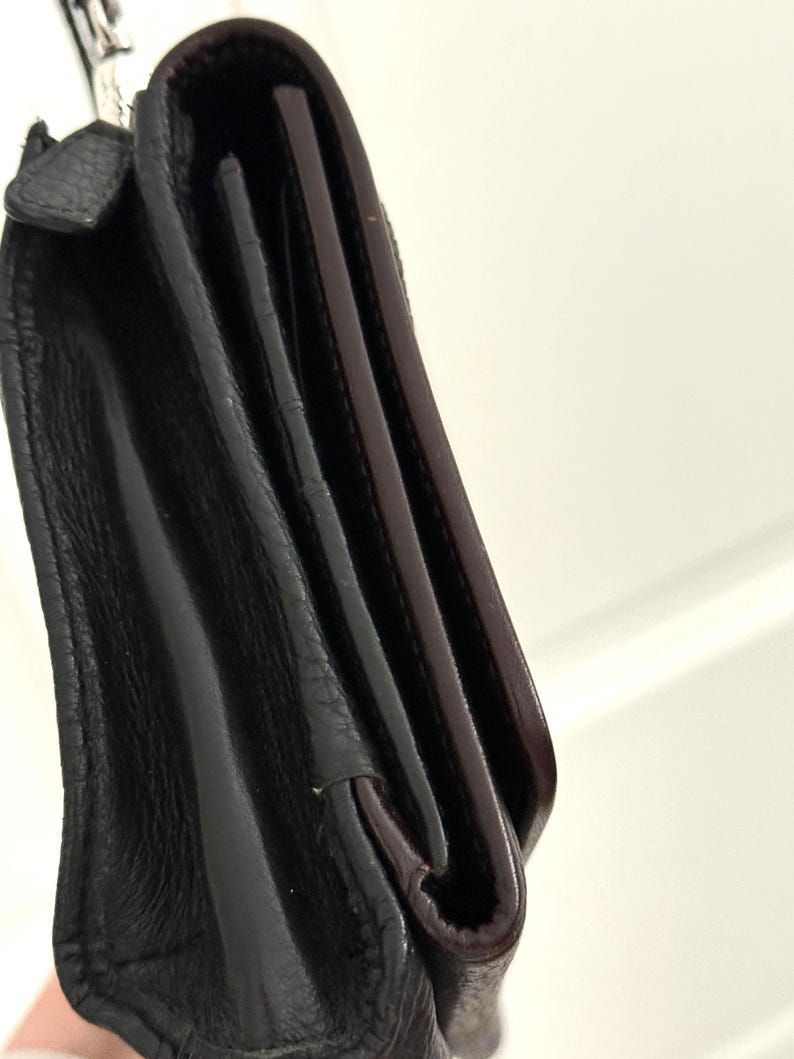 May include: Close-up of a black leather wallet with a silver chain. The wallet is folded, revealing a glimpse of the interior with a dark brown lining. The leather has a textured appearance.