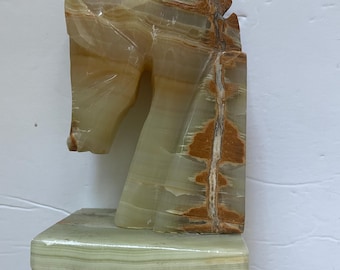 May include: A green and brown onyx horse head bookend. The horse head is carved from a single piece of onyx and has a detailed mane and face. The bookend is mounted on a square base.