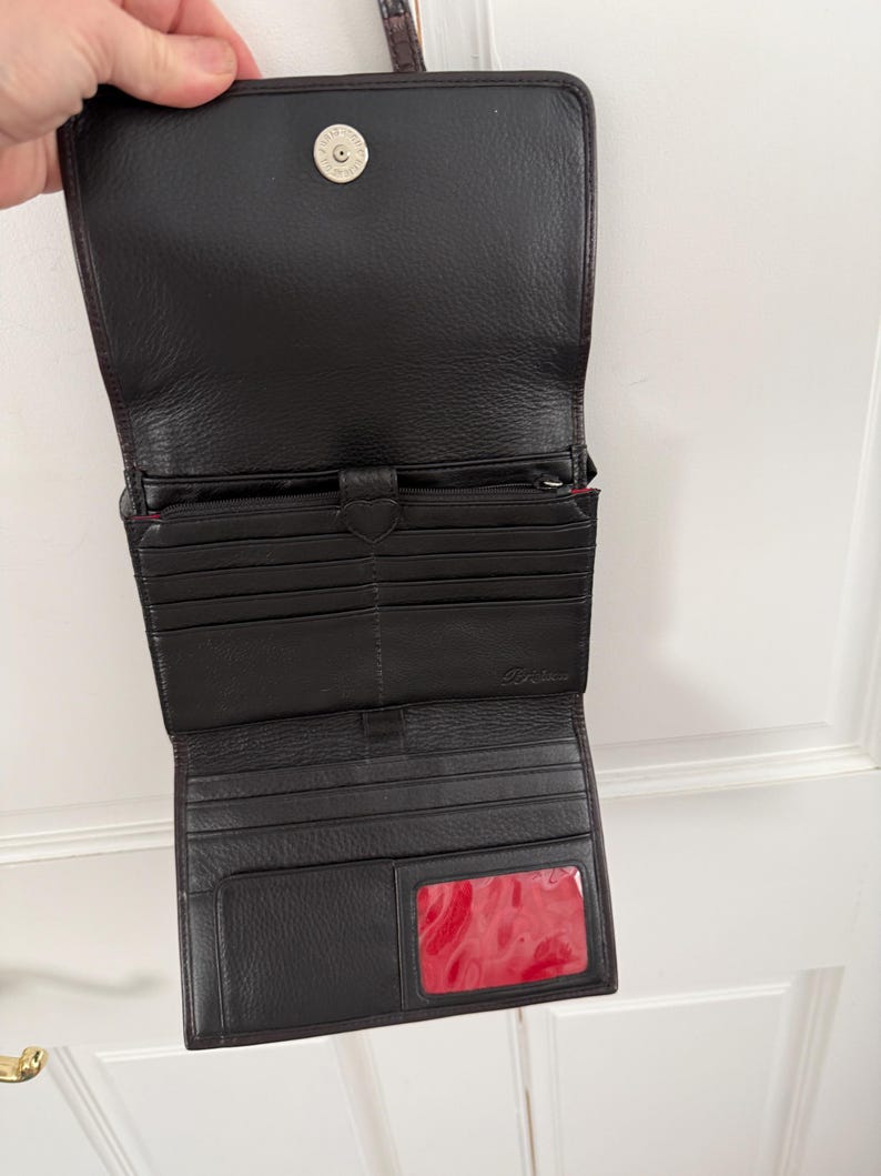 May include: Open black leather wallet with multiple card slots, a zippered compartment, and a clear ID window with a red interior. The wallet has a magnetic snap closure and a small metal accent.