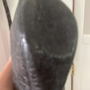 Puede incluir: Un bolso de mano gris oscuro texturizado con una correa trenzada. El bolso parece estar hecho de un material suave y tiene una forma redondeada. La correa es de color marr&oacute;n oscuro.