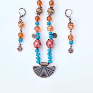 May include: A necklace and earring set featuring orange, turquoise, and brown beads. The necklace has a half-circle pendant. The earrings and necklace have spiral charms. The jewelry is displayed on a white surface.