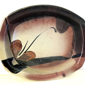 May include: Handmade ceramic serving dish with a rectangular shape. The dish features a speckled beige interior with brown and black abstract designs. The rim is dark brown, and the exterior has a reddish-brown hue.