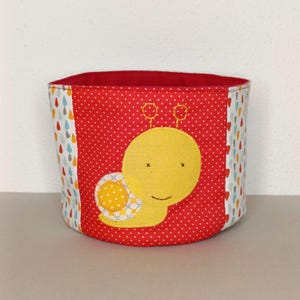 Peut inclure: Un bac de rangement en tissu avec un motif de pois rouges et une application d'escargot jaune. L'intérieur est rouge et les côtés présentent un motif de gouttes colorées. Un récipient charmant et fonctionnel.