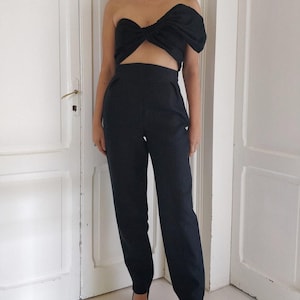 Puede incluir: Conjunto negro de dos piezas que consta de un top sin tirantes con detalle de lazo y pantalones de cintura alta. El conjunto se combina con tacones negros de punta. Adecuado para eventos formales o una salida nocturna.