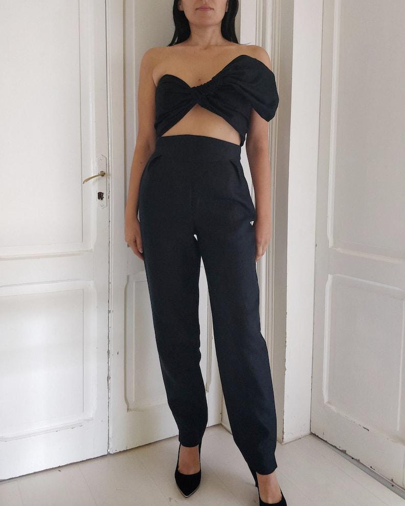 Puede incluir: Conjunto negro de dos piezas que consta de un top sin tirantes con detalle de lazo y pantalones de cintura alta. El conjunto se combina con tacones negros de punta. Adecuado para eventos formales o una salida nocturna.