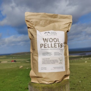 May include: A brown paper bag with a white label that says "Sheep Unique Wool Pellets" and "Fertilise your plants, reduce watering and repel slugs". The bag is sitting on a wooden fence post with a green field and blue sky in the background.