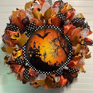 May include: A Halloween wreath with a black and white polka dot ribbon, orange and gold mesh, and a black silhouette of a haunted house with a full moon and bats on a dark orange background.