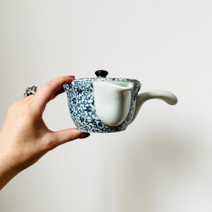 May include: A blue and white ceramic teapot with a floral pattern and a white spout. The teapot has a black knob on the lid.