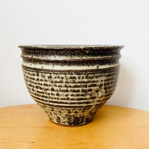 May include: A brown and white ceramic planter with a textured surface. The planter has a wide base and a narrow opening.