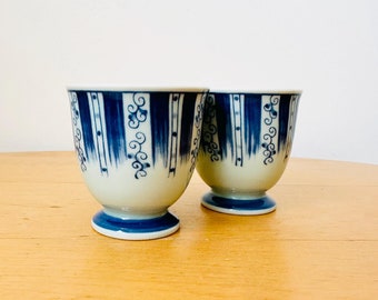 Könnte beinhalten: Zwei weiße Keramikbecher mit blau-weißem Muster. Die Becher haben eine ausgestellte Form und einen kleinen Fuß.