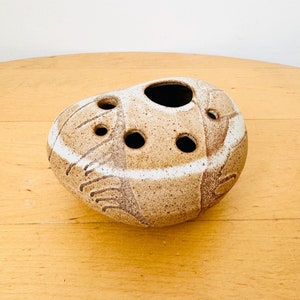 Könnte beinhalten: Eine braune und weiße Keramikvase mit abgerundeter Form und mehreren Löchern für Blumenstiele. Die Vase hat eine gesprenkelte Glasur und ein weißes Design.