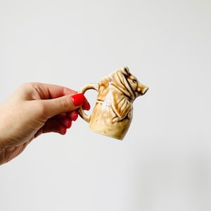 Könnte beinhalten: Ein kleiner Keramik-Milchkännchen in Form eines Bären. Der Milchkännchen ist braun und weiß mit einem detaillierten Design.