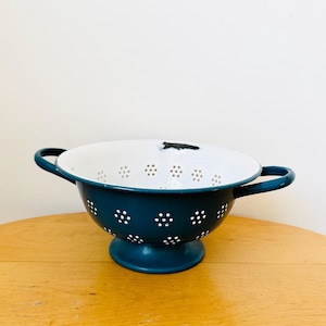 May include: A teal blue enamel colander with white polka dots and two handles. The colander has a white interior and a white base.