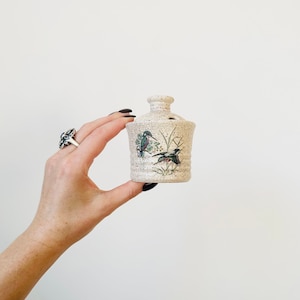 May include: A small, white ceramic incense burner with a bird and floral design. The burner has a round body and a small opening on top.