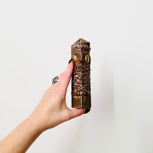 May include: A brown ceramic owl-shaped incense holder with yellow glass eyes. The holder is textured and has a triangular top.
