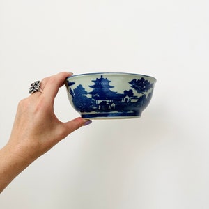 Könnte beinhalten: Eine weiße Keramikschüssel mit einem blauen und weißen Design aus einer Pagode und Bäumen. Die Schüssel ist handbemalt mit einem traditionellen chinesischen Design.