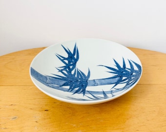 May include: A white ceramic bowl with a blue and white bamboo design. The bowl is round and has a slight lip.