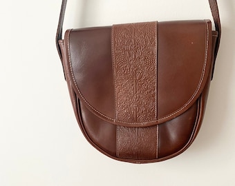 May include: A brown leather shoulder bag with a flap closure and an embossed floral design on the front.