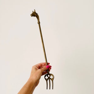May include: A brass fireplace tool with a horse head handle and a three-pronged fork.