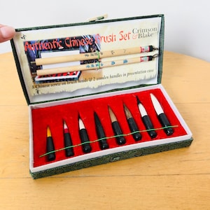 Op de afbeelding: Een authentieke Chinese penseelset van Crimson & Blake in een groen gedessineerde presentatiekoffer. De set bevat twee lichtgekleurde houten handvatten en acht opschroefbare penseelkoppen met diverse haarkleuren en formaten op rood fluweel.