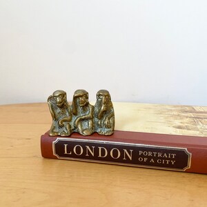 May include: Three brass monkey figurines sitting on a book titled "London Portrait of a City".