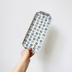 May include: A white ceramic serving tray with a blue and green floral pattern. The tray has a rectangular shape with rounded corners and a slightly raised edge.