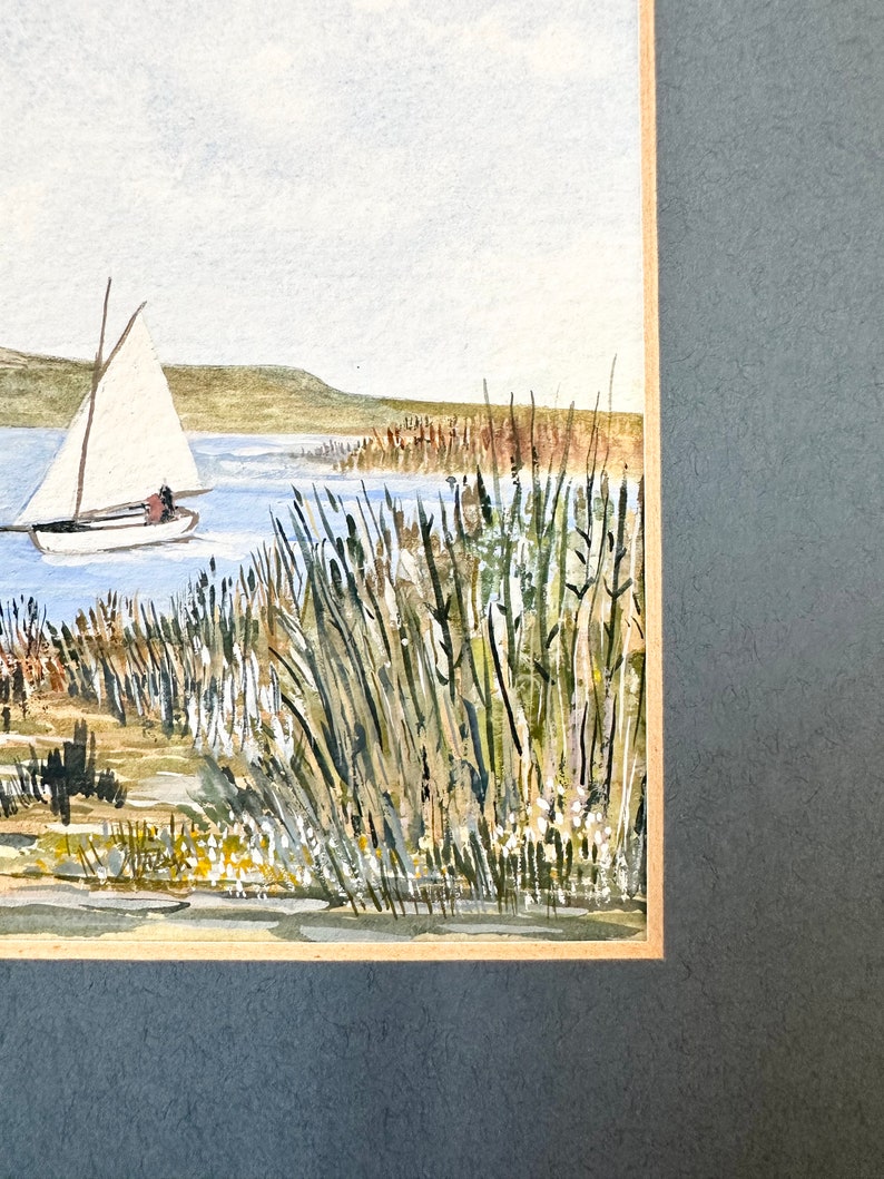 Puede incluir: Pintura acuarela de un velero en un lago con altas ca&ntilde;as verdes en primer plano. El cielo es azul claro y el agua es azul verdoso claro.