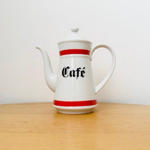 Può includere: Caffettiera in ceramica bianca con una fascia rossa e la scritta "Cafe" in lettere nere.