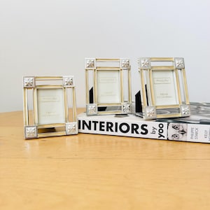 May include: Three silver picture frames with a gold trim and a white background. The frames are sitting on a book titled "Interiors by yoo".