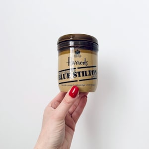 Puede incluir: Un tarro de cerámica marrón con tapa. El tarro tiene una etiqueta que dice "Harrods Finest Selected Blue Stilton Cheese".