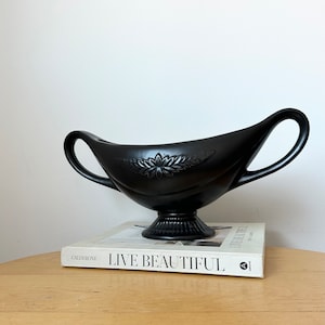May include: A black ceramic bowl with two handles and a floral design. The bowl is sitting on a book titled "Live Beautiful" by Calderone.