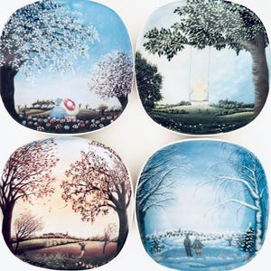 May include: Four square decorative plates with seasonal landscape scenes. Each plate features a different season: spring, summer, autumn, and winter. The plates depict trees, people, and various outdoor settings in a colorful, artistic style.