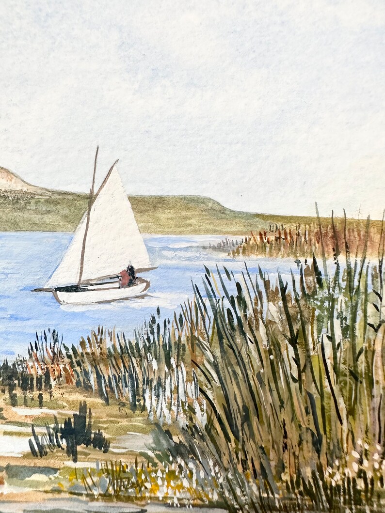 Puede incluir: Una pintura de acuarela de un velero en un lago con altas ca&ntilde;as verdes en primer plano. El velero tiene una vela blanca y navega lejos del espectador. El lago es de color azul claro y el cielo es de color gris claro.