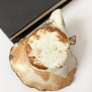 K&ouml;nnte beinhalten: Eine kleine, wei&szlig;e Keramikschale mit brauner Glasur. Die Schale hat einen gewellten Rand und eine leicht unregelm&auml;&szlig;ige Form. Der Boden der Schale ist sichtbar und zeigt eine braune Markierung.