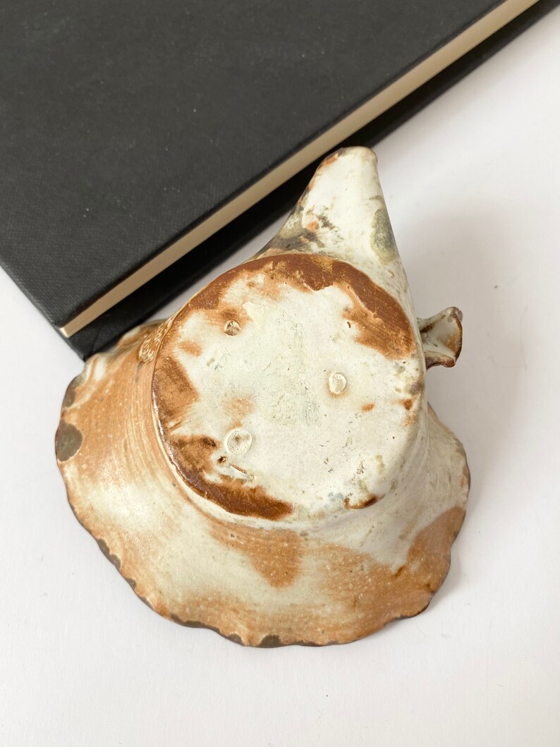 K&ouml;nnte beinhalten: Eine kleine, wei&szlig;e Keramikschale mit brauner Glasur. Die Schale hat einen gewellten Rand und eine leicht unregelm&auml;&szlig;ige Form. Der Boden der Schale ist sichtbar und zeigt eine braune Markierung.