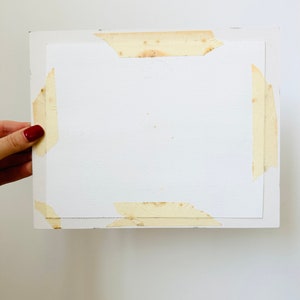 Puede incluir: Una hoja de papel rectangular blanca pegada a una superficie blanca. El papel tiene algunas manchas marrones y est&aacute; pegado por los cuatro lados.