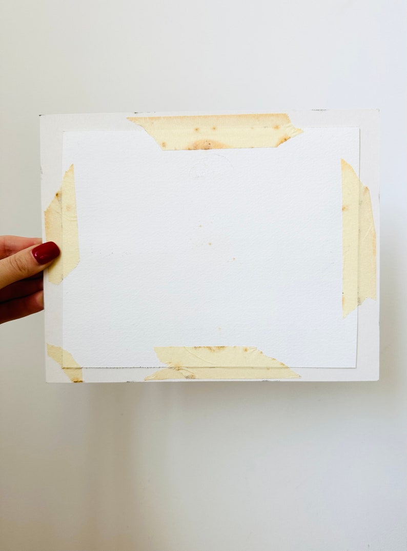 Puede incluir: Una hoja de papel rectangular blanca pegada a una superficie blanca. El papel tiene algunas manchas marrones y est&aacute; pegado por los cuatro lados.