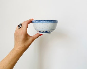 May include: A white ceramic bowl with a blue and white floral pattern. The bowl is being held in a hand.
